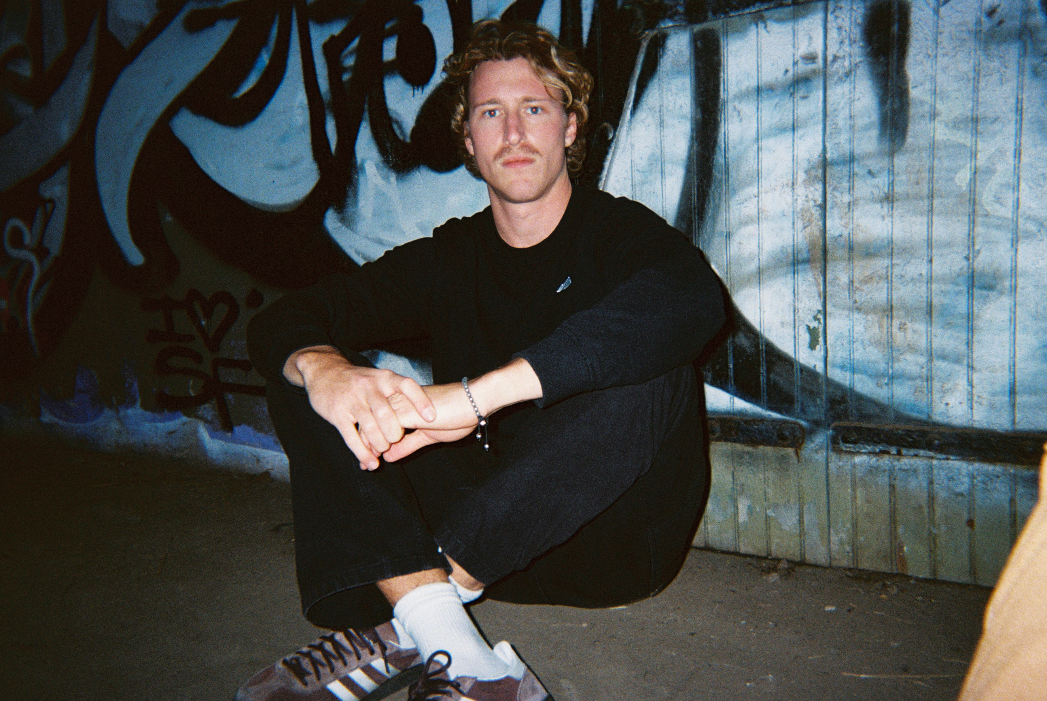 Max Fuster seated against a graffiti wall at night